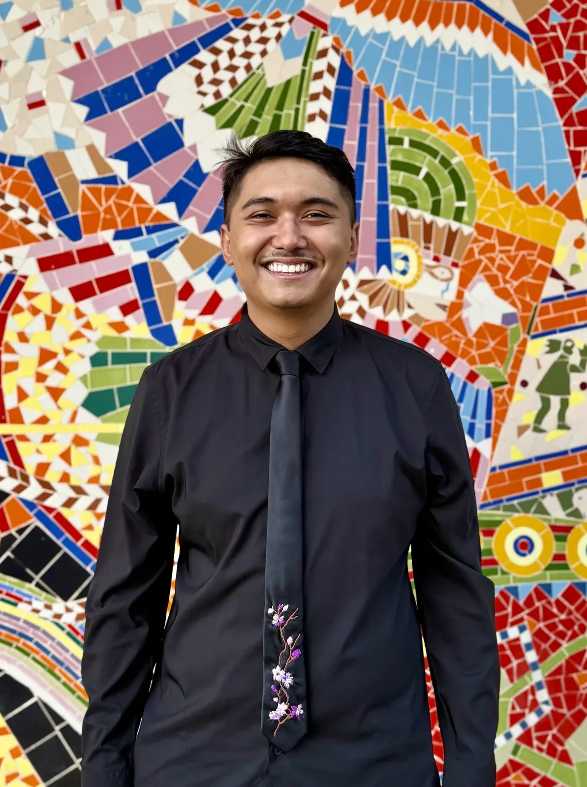 Retrato com gravata bordada de flores de cerejeira, diante de um mural de mosaico